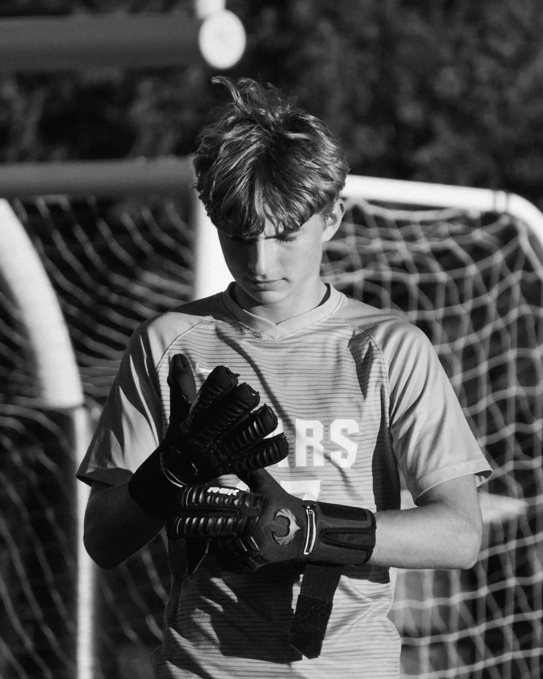 Black-and-white portrait of a soccer goalkeeper adjusting his gloves in front of the goal