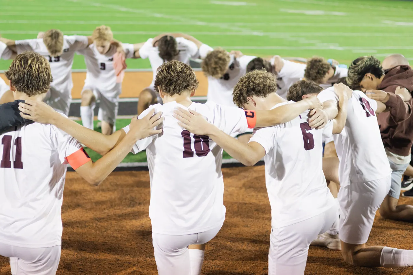 Soccer team gathered in a full huddle with arms around each other's shoulders