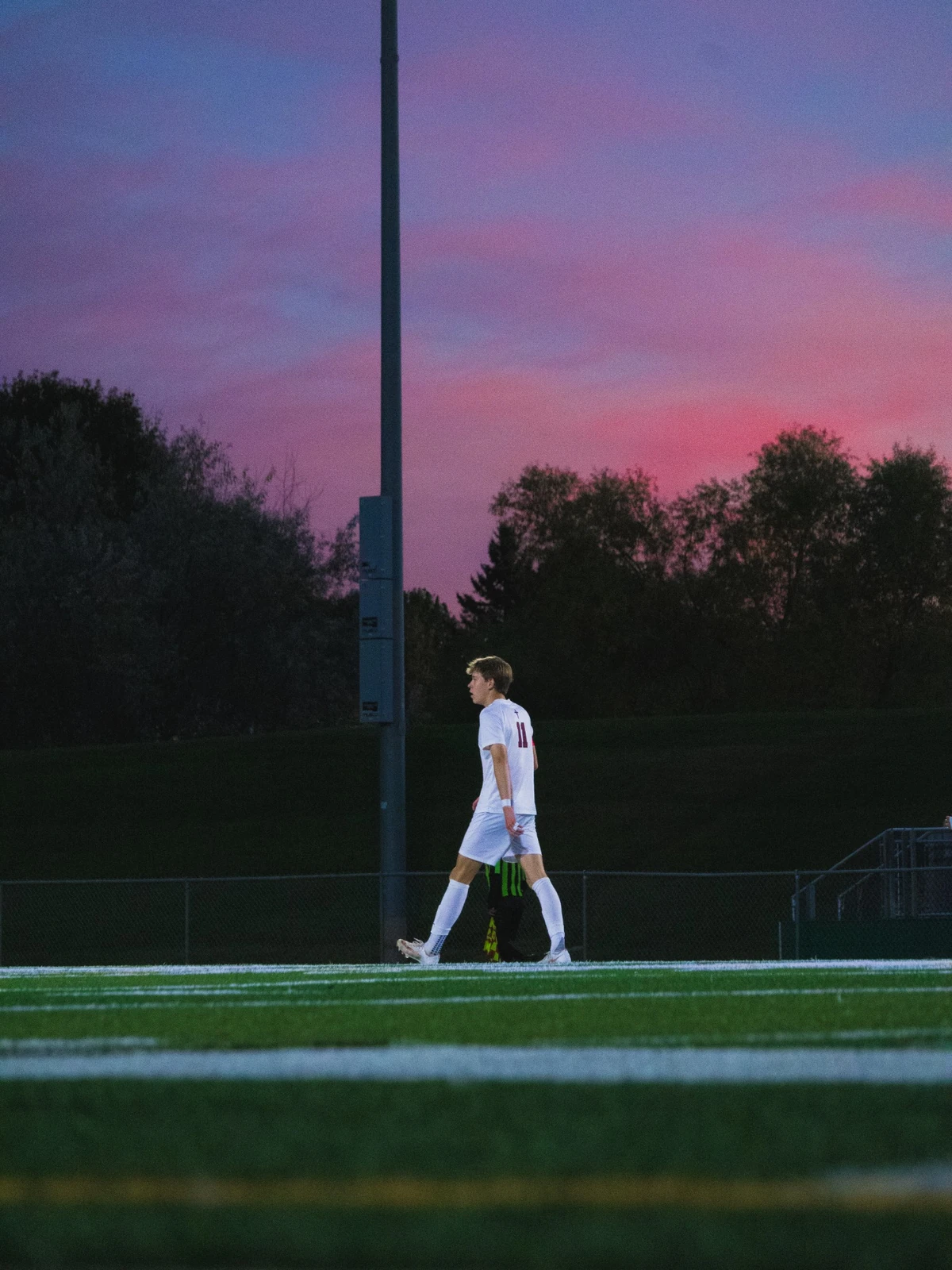 Soccer player walking across the field beneath a pink and purple sunset